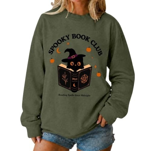 Olive green sweatshirt with a cat in a witch hat sitting on a stack of books