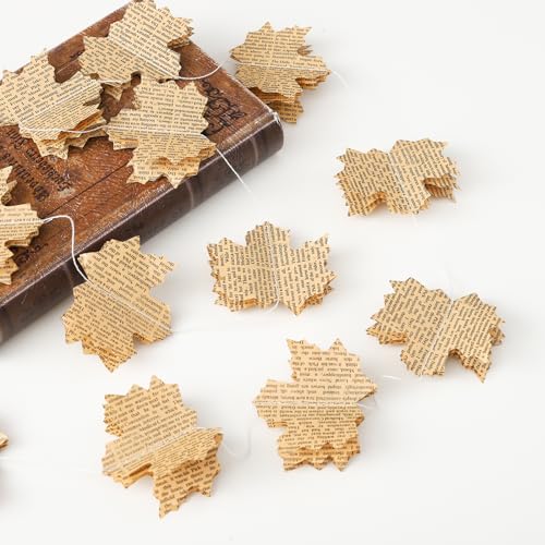 Maple leaves cut from aged printed book pages, strung on fine twine beside an antique leather book