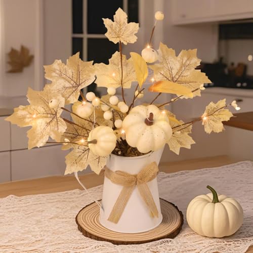 Cream maple leaves, white pumpkins and berry stems arranged in a small white metal pitcher with warm lights inside
