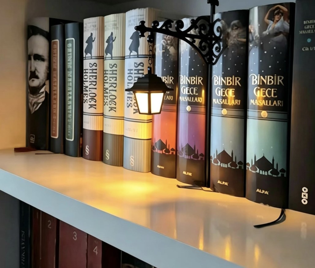 Miniature wrought iron street lamp clipped to a shelf edge glowing over a row of books